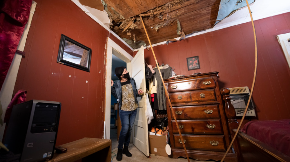 A woman looks up at the damage in her ceiling. Boards are being used to prop up ceiling sections.