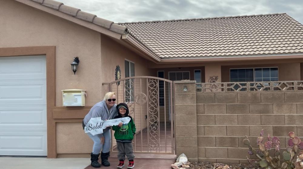 A woman and her son stand outside their newly purchased home, holding a giant key.