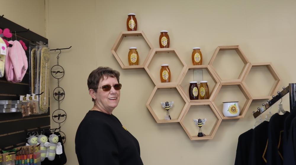 Smiling woman standing in a shop with honey and honey-themed products on shelves on the walls and on racks.