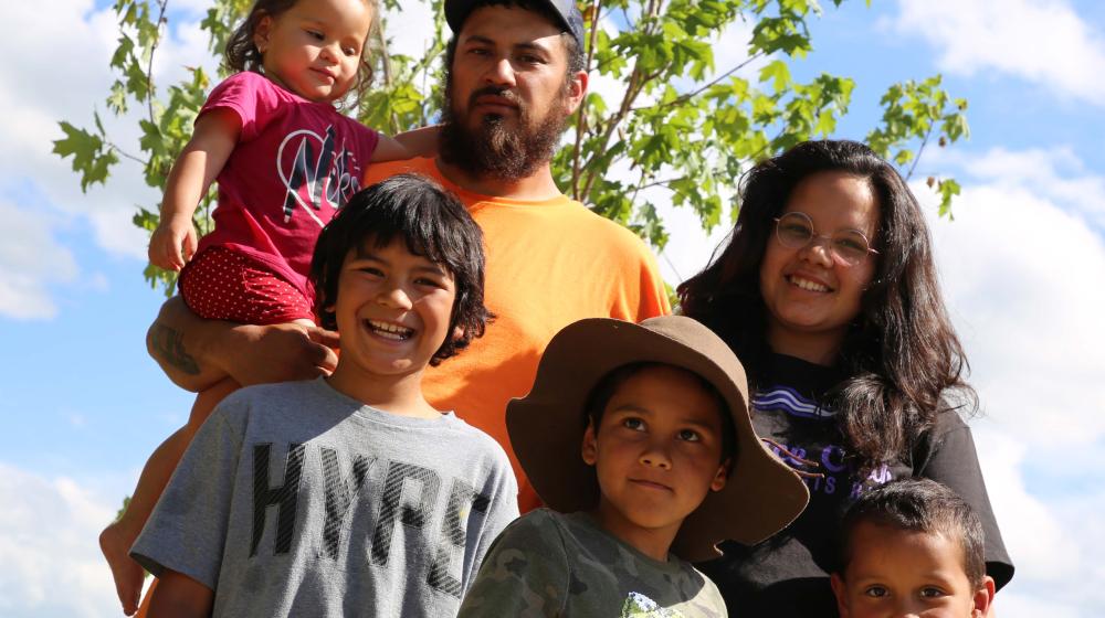 The Thompson Family, father, mother, four children, posing in front of a maple tree planted during a recent USDA Homeownership Month Event in their new backyard along the Raquette River.