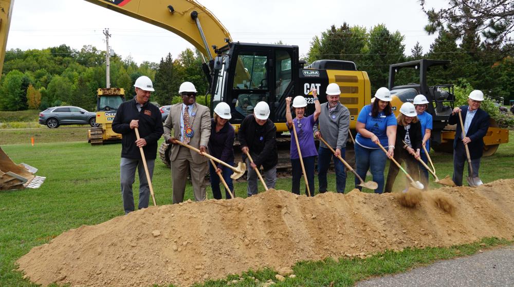 A group of people are standing in a line with shovels at a groundbreaking event.