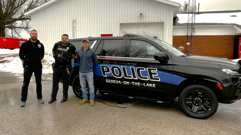 Three men standing next to a police equipped sport utility vehicle.