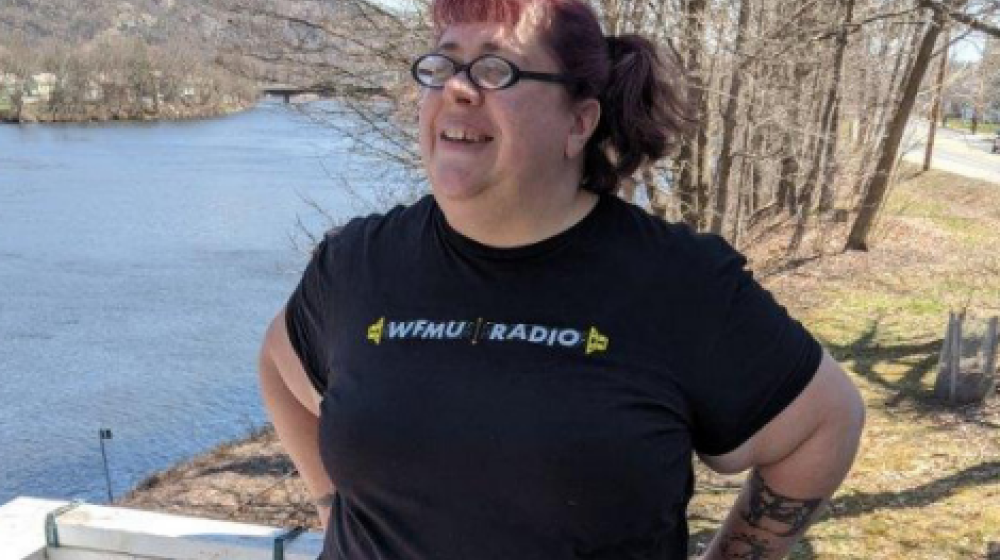 Smiling woman standing next to a river. Trees in the background.