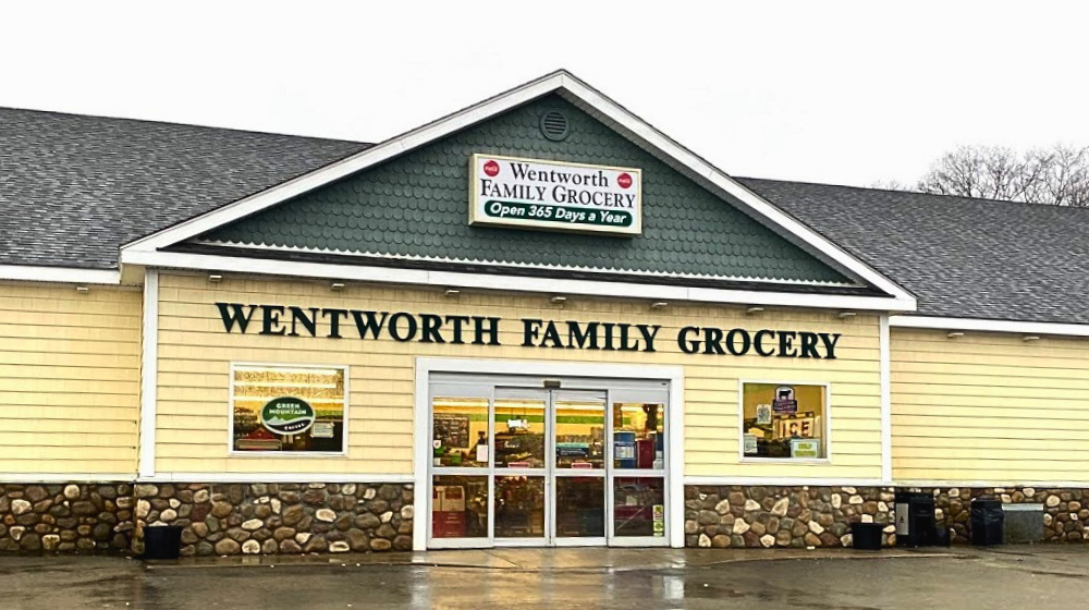 Wentworth Family Grocery is a long, low building with yellow siding, large glass doors, and stone trim around the base of the building.