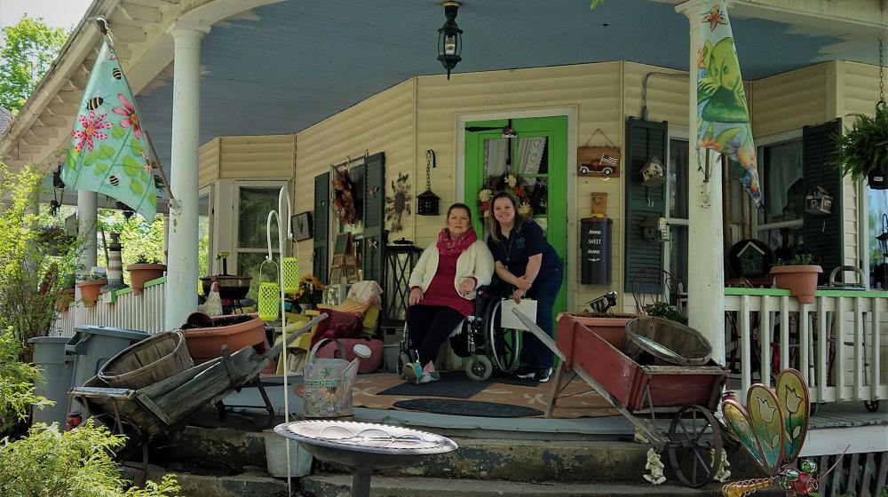 Two smiling women on porch of a large old home with wrap around porch