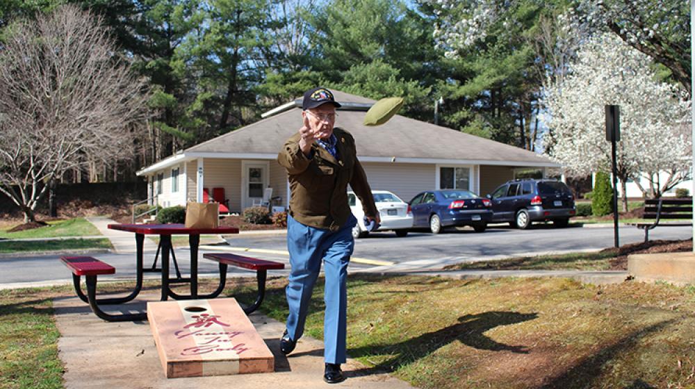 Henry Smith, wearing his World War II uniform coat because he had just had pictures taken in it, plays the lawn game Cornhole at Milnwood Village Apartments in Farmville.