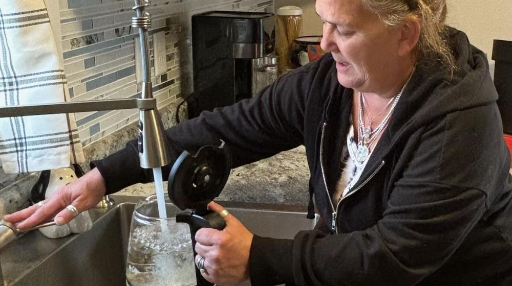 Woman fills coffee pot with water in sink