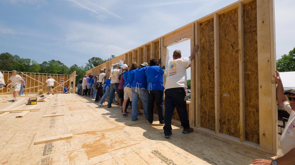 Several people raise a house wall during a group construction project