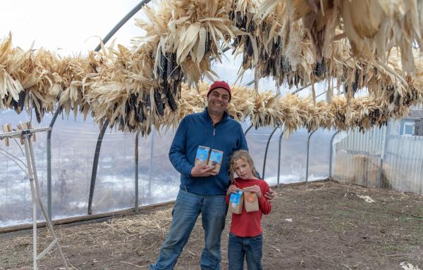 Man and child standing under corn hung to dry