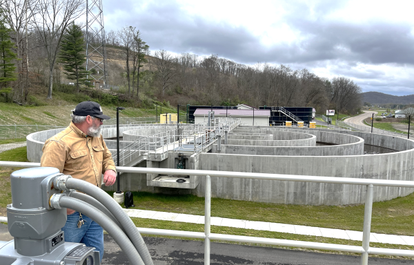 Man standing by wastewater plant in rural area. 