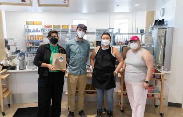 Four people stand in front of a café counter