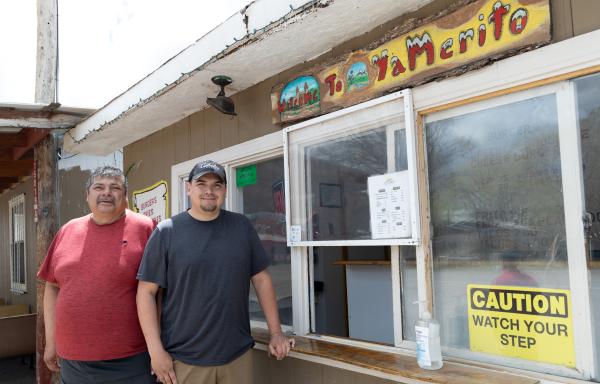 Two men stand to the left of an outside restaurant order window