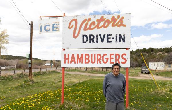 Man standing in front of Victor's Drive-In, Hamburgers sign