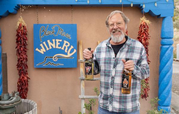 Man holding two bottles of wine in front of Black Mesa Winery sign