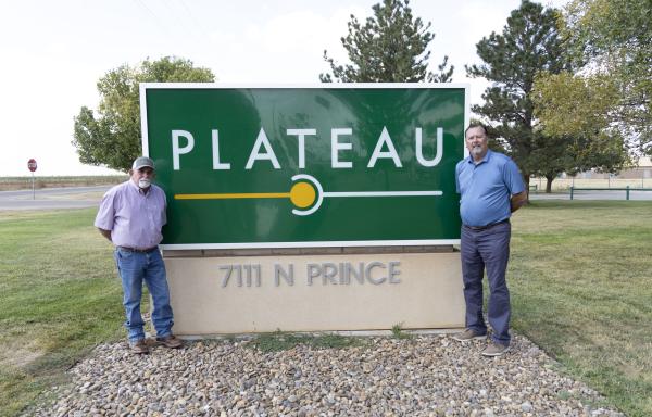 Two men stand next to a green sign that says Plateau