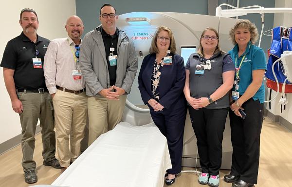 Three men and three women pose in front of a CT machine at CA Dean hospital. 