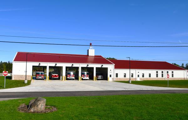 Rural fire station with trucks visible in five open bays. 
