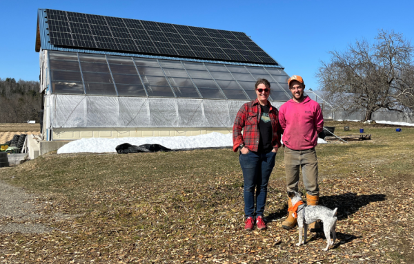 Molly and Everett pose with dog Cricket in front of their barn with the solar panels on the roof.