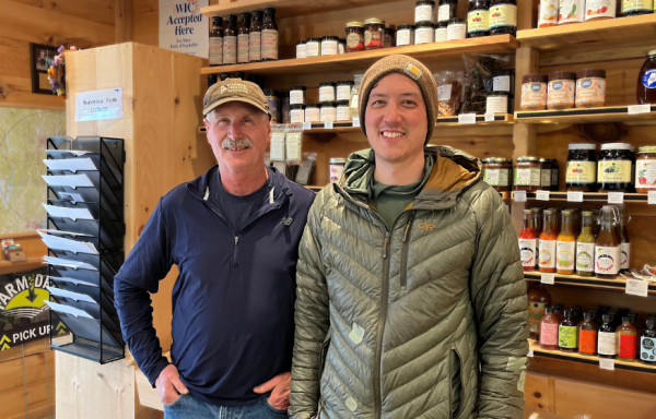 Owner Gary and manager Eric of Replenova Farm pose inside the farm store, with shelves of local foods arrayed behind them.