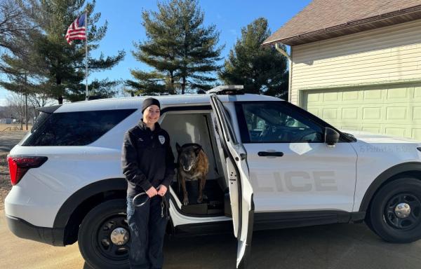 A police officer stands beside a police car with a police dog