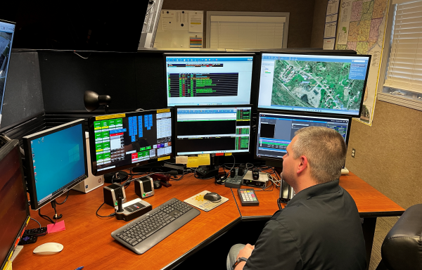 Man sitting at desk in front of many computer screens.