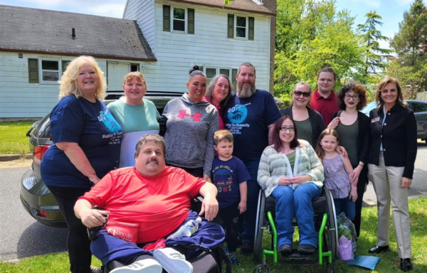 Family standing on the lawn in front of a white two-story house. Two family members are in wheelchairs.