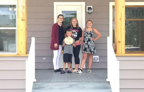 A USDA loan specialist stands on the steps of a house with the new homeowner and her family