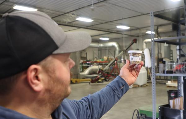 Jared Stober with an outstretched hand holding a small bottle with grains inside.