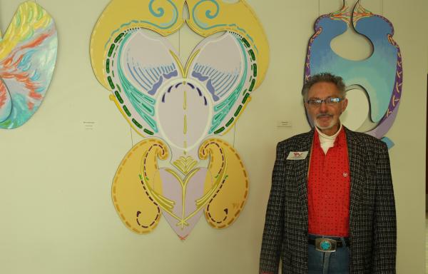 Artist John Welch standing in front of his colorful art in an exhibit.