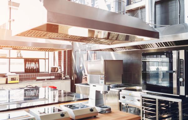A sunny industrial kitchen with equipment, a hood over a range, and ovens. 
