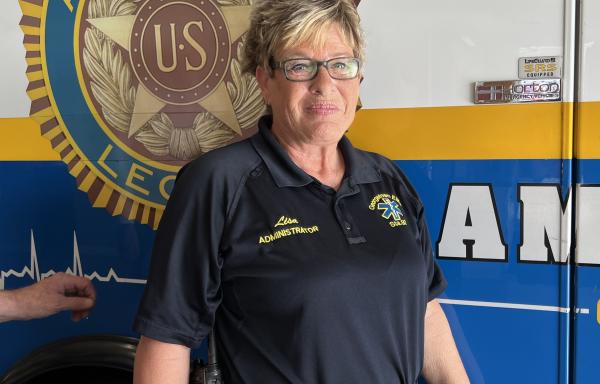 Smiling woman named Lisa Fensick standing in front of a new ambulance she helped obtain for her fire station.