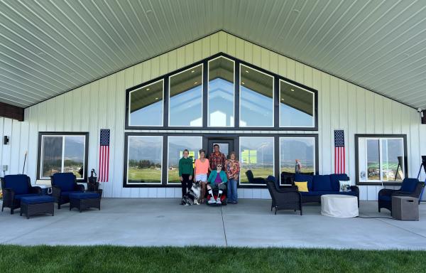 A group of residents stands outside a senior center on a cement patio. Large picture windows are behind them.