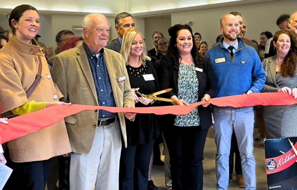Smiling people hold a ribbon inside the Maine Arts Academy during the official ribbon-cutting ceremony.