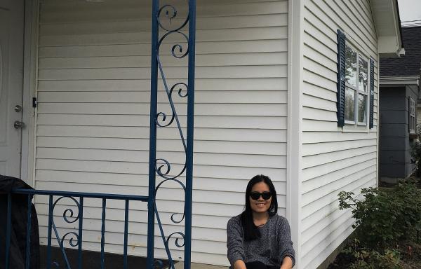 Smiling woman sitting on the brick front steps of a while house.