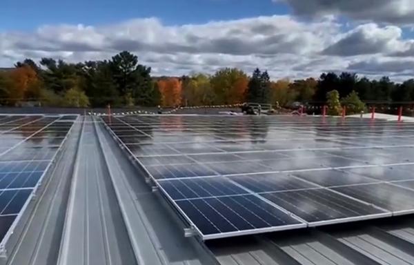 A solar array on the top of a roof with fall colors in the trees behind