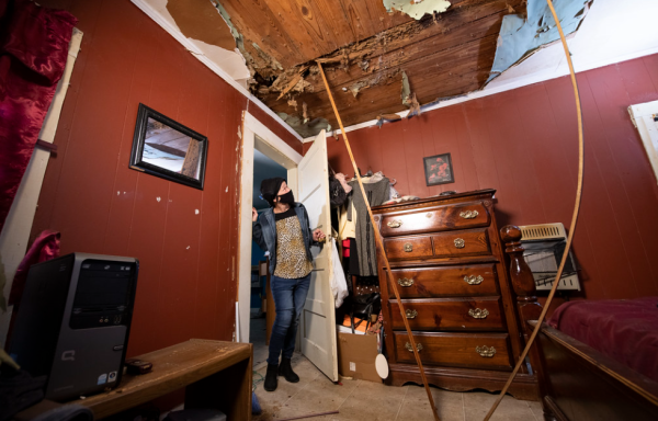 A woman looks up at the damage in her ceiling. Boards are being used to prop up ceiling sections.