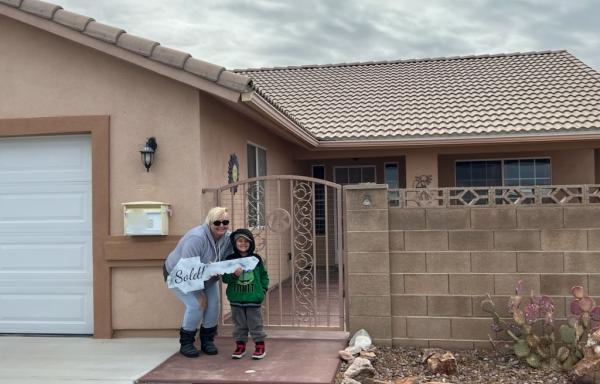 A woman and her son stand outside their newly purchased home, holding a giant key.
