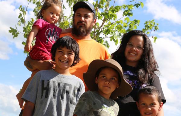 The Thompson Family, father, mother, four children, posing in front of a maple tree planted during a recent USDA Homeownership Month Event in their new backyard along the Raquette River.