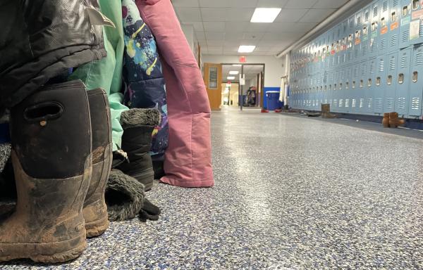A hallway at a rural elementary school shows snowpants and boots across from a wall of blue lockers.