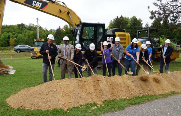 A group of people are standing in a line with shovels at a groundbreaking event.