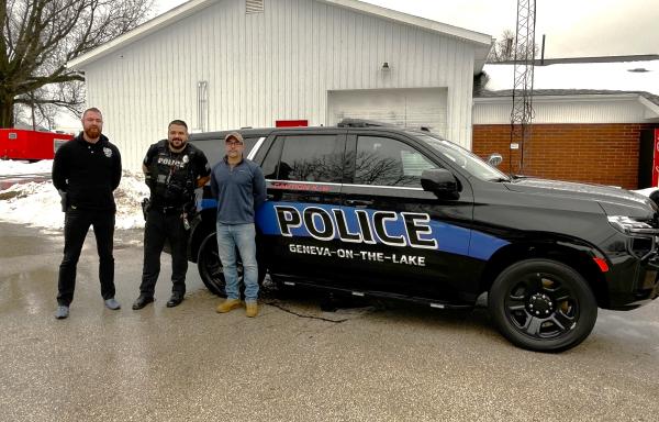 Three men standing next to a police equipped sport utility vehicle. 
