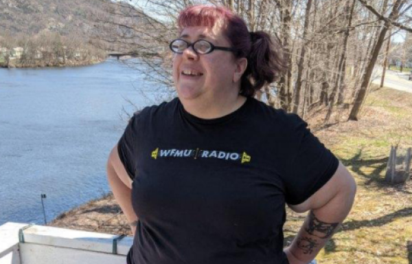 Smiling woman standing next to a river. Trees in the background.