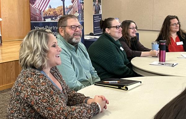 Four women and one man sit at tables in a large room with a USDA banner in the background.