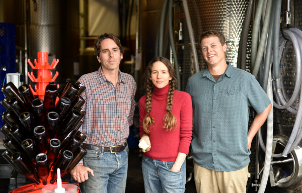 finnriver coowners photo by james curtis. Three people smiling in front of fermenting equipment and bottles.