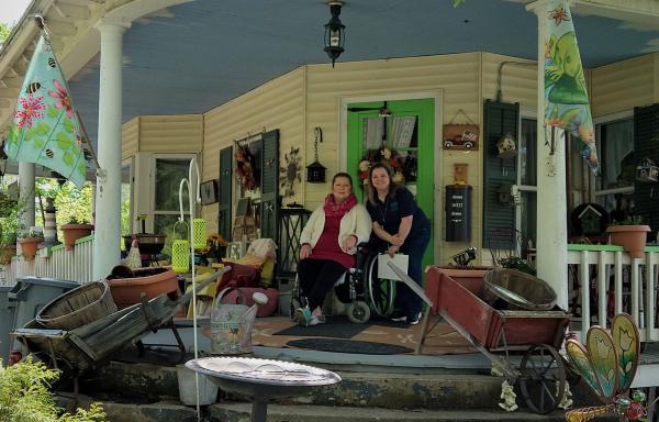 Two smiling women on porch of a large old home with wrap around porch