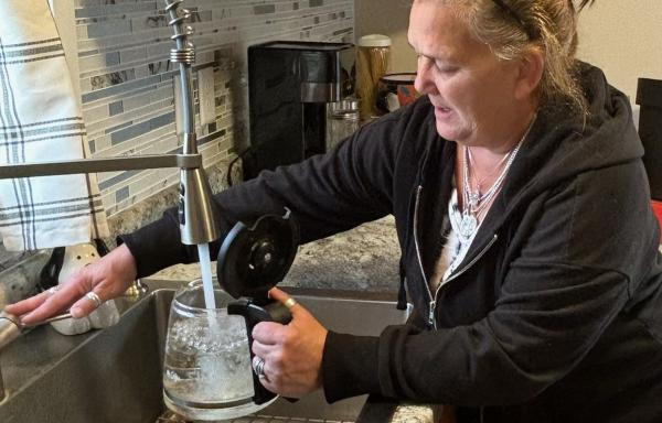 Woman fills coffee pot with water in sink