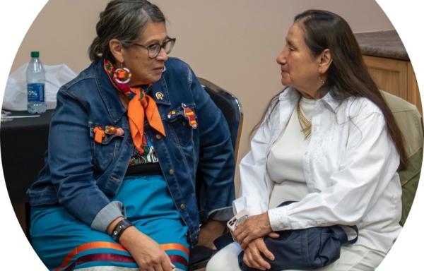 Native American ladies sitting in chairs, talking and smiling with each other.