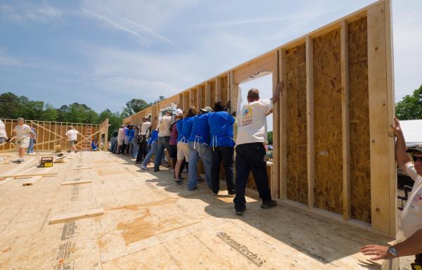Several people raise a house wall during a group construction project