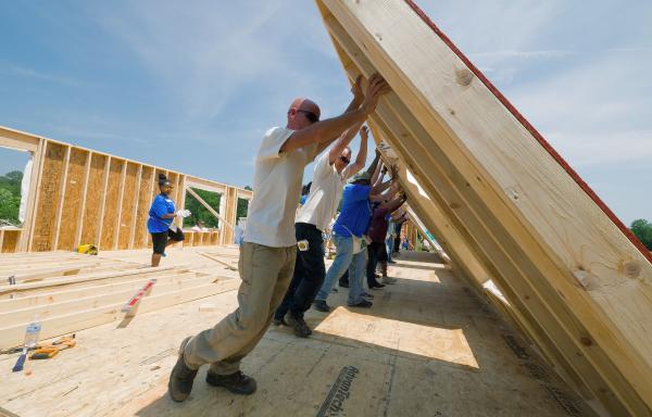 Photo of people lifting up a wall frame they have built out of wood while building a house.