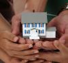 This is an image of a small house being held by several hands.